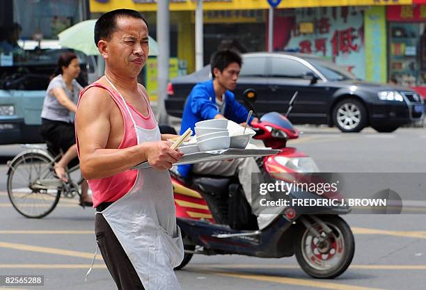 Restaurant worker carries a tray of bowls and dishes while crossing a street in Chengdu on August 25, 2008 in southwest China's Sichuan province....
