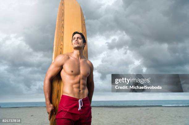 hispanic surfer with a dramatic sky at the ocean - board shorts stock pictures, royalty-free photos & images