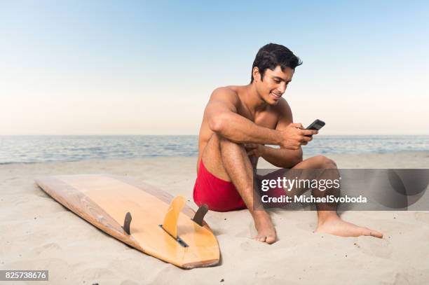 hispanic surfer checking his smart phone - board shorts stock pictures, royalty-free photos & images