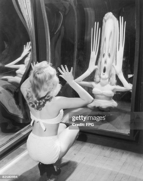 Woman in a towelling bikini poses in a funfair hall of mirrors, circa 1935.