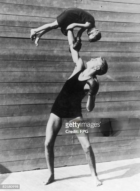 Boxer holds a small boy in the air, circa 1935.