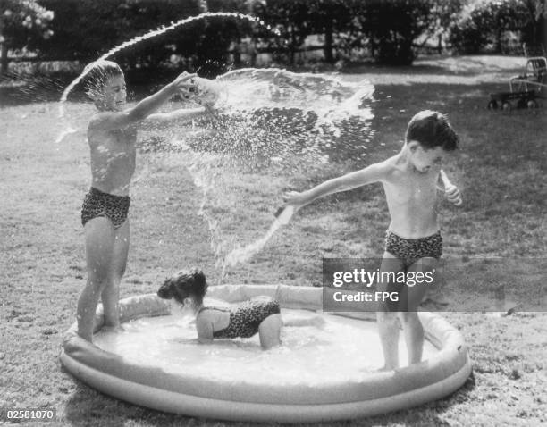 Three children in leopardskin swimsuits splash around in a paddling pool, circa 1950.