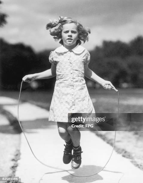 Little girl bounces down a pathway with a skipping rope, circa 1940.