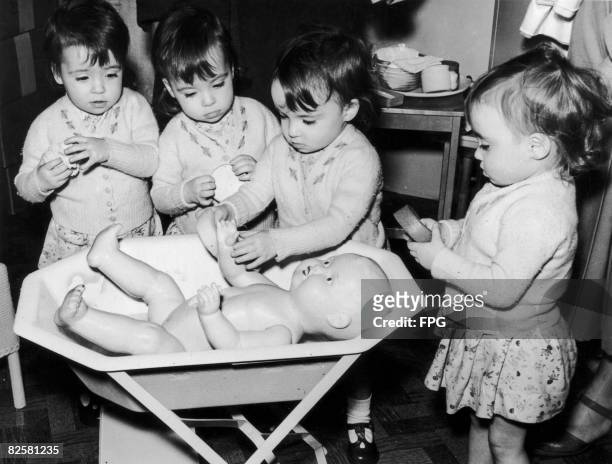 Circa 1940, The two-year-old Cole quadruplets learn to bathe a large doll at the Mothercraft exhibition in London's Central Hall.