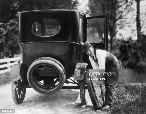 Man repairing a flat tyre on a Model T Ford, circa 1925.