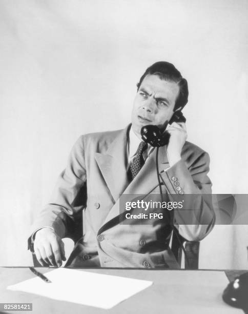 Businessman in a double-breasted jacket makes a telephone call, circa 1950.