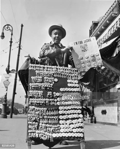 Young man stands with a placard full of buttons, including 'I'm for Jackie' ones, commemorating Jackie Robinson becoming the first African-American...
