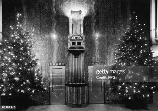 Photograph shows the interior of the lobby of the Chrysler Building and its clock, two doors, and two Christmas trees with strings of light, the wall...