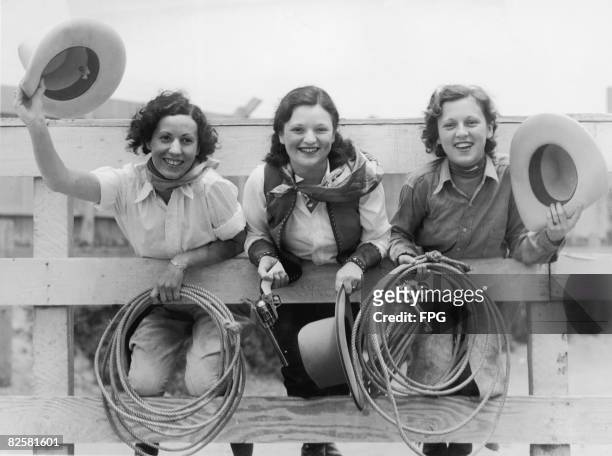 At a rodeo, from left, Cecelia Ashadina, Aleen Thompson, and Dorothy Abbott lean on a railing and pose for a picture, 1930s.