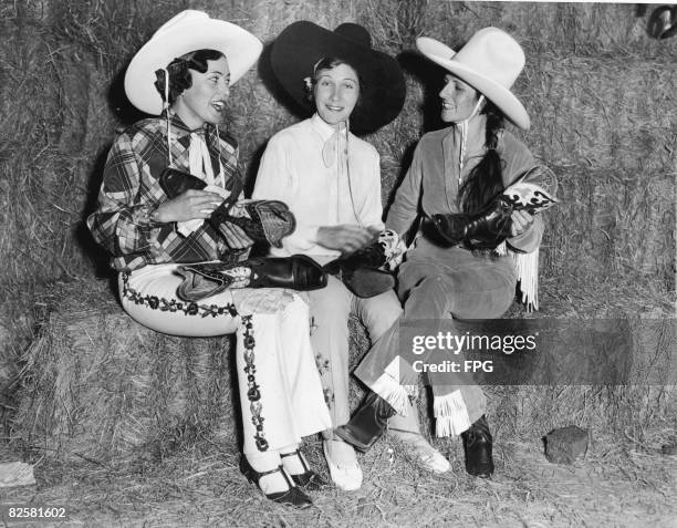 Three American cowgirls, from left, Lucyle Roberts , Alice Greenough , and Reine Shelton , sit on haybales, polishing and comparing boots in...