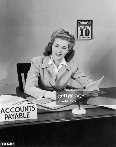 An office worker makes an entry in a ledger, circa 1945.