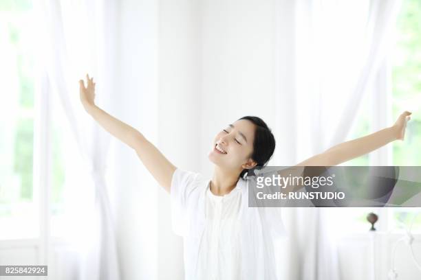 woman outstretching arms by window - stretching ストックフォトと画像