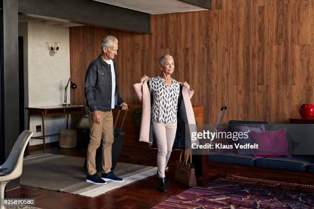 mature couple arriving to rental flat, with suitcases and bag - taking off coat stock pictures, royalty-free photos & images