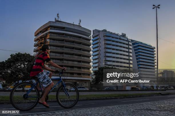 Man rides his bike in front of an hotel that became a residense after Rio 2016 Olympic Games on Praia da Barra in Rio de Janeiro on August 3, 2017....