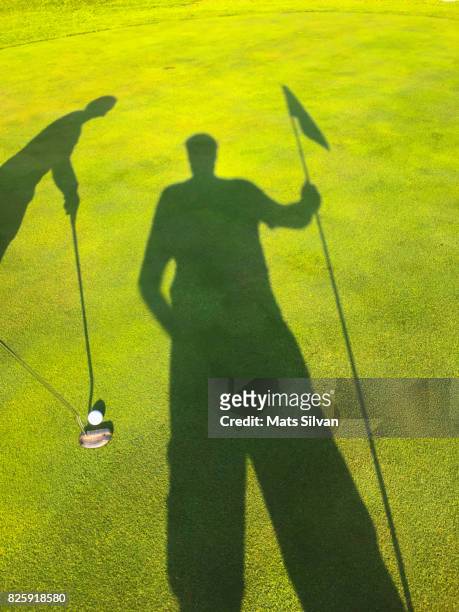 shadow of a woman and a caddy putting on golf course - golf caddy stockfoto's en -beelden