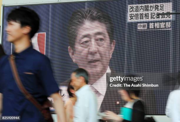 People walk past a giant screen broadcasting the news of Prime Minister Shinzo Abe reshuffling his cabinet on August 3, 2017 in Osaka, Japan. Prime...