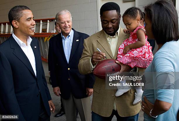 Pittsburgh Steelers head coach Mike Tomlin autographs a football while holding his daughter, Harlyn Quinn, for Democratic Presidential Candidate...