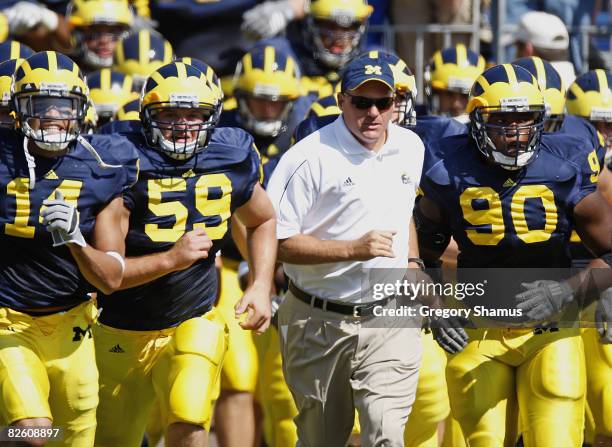 Head coach Rich Rodriguez of the Michigan Wolverines leads his team onto the field between Tim Jamison and Sean Griffin prior to playing the Utah...