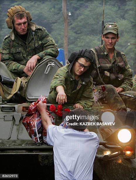 Man gives a plastic bag and flowers to Russian soldiers as they leave South Ossetia at the North-South Ossetia border some 60 km outside Vladikavkaz...