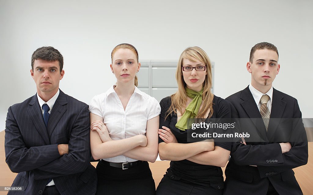 Four businesspeople sitting on desk in office