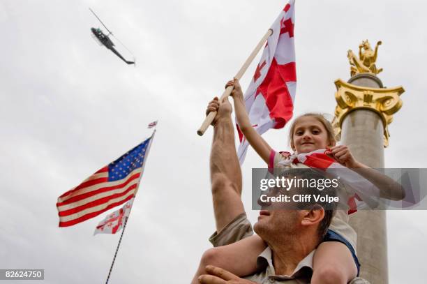 An American-made UH-1 "Huey" helicopter belonging to the Georgian military flies over a peace rally held in Republic Square, where a golden statue of...