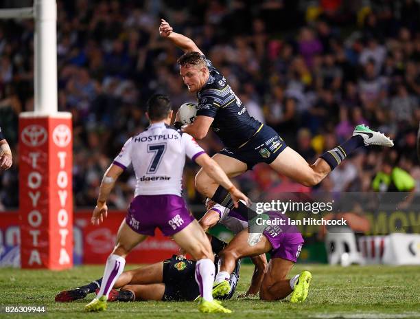 Coen Hess of the Cowboys jumps over Will Chambers of the Storm and is then tackled by Cooper Cronk of the Storm during the round 22 NRL match between...