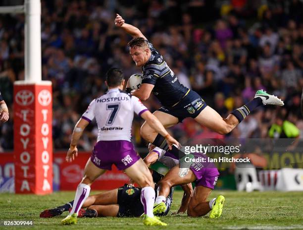 Coen Hess of the Cowboys jumps over Will Chambers of the Storm and is then tackled by Cooper Cronk of the Storm during the round 22 NRL match between...