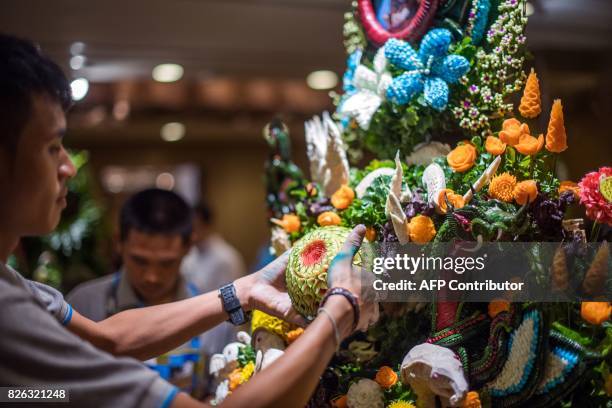 Thai man helps put together an elaborate decoration with carved fruits and vegetables during a fruit and vegetable carving competition in Bangkok on...