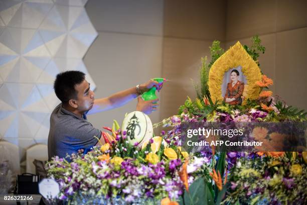 Worker sprays water on an elaborate fruit and vegetable decoration adorned with the photograph of Thailand's Queen Sirikit during a fruit and...