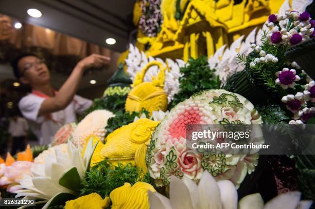 Thai man helps put together an elaborate decoration display with carved fruits and vegetables during a fruit and vegetable carving competition in...