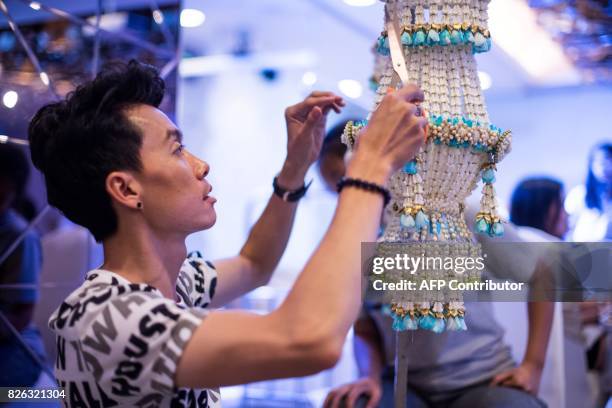 Thai man helps put together an elaborate decoration during a fruit and vegetable carving competition in Bangkok on August 4, 2017. It is a royal...