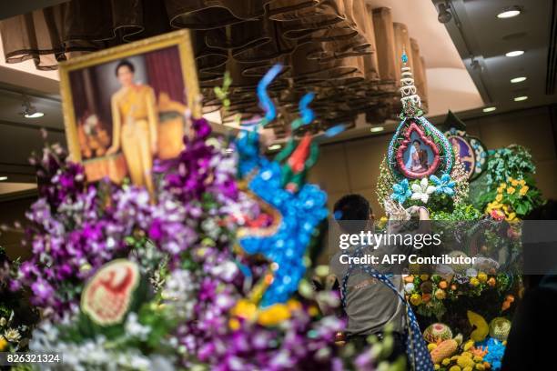 Thai man helps put together an elaborate decoration with carved fruits and vegetables adorned with images of Thai Queen Sirikit, during a fruit and...