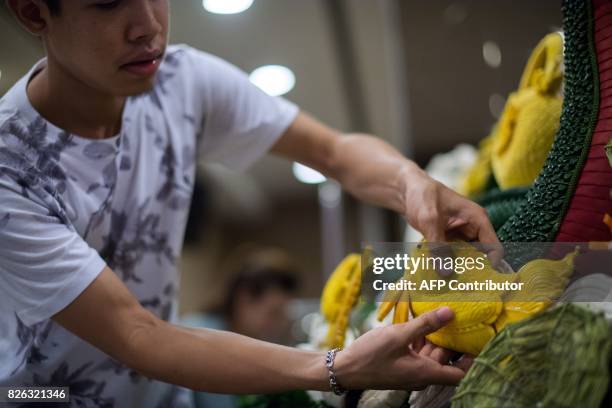 Man adds a pumpkin carved in the shape of a fish to an elaborate display during a fruit and vegetable carving competition in Bangkok on August 4,...