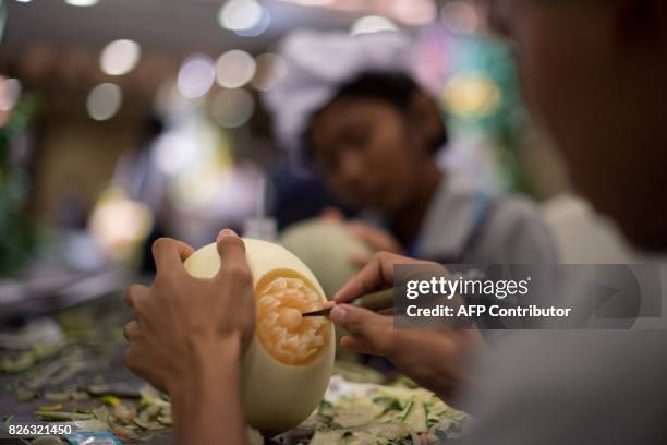 Thai girl carves floral patterns into a melon during a fruit and vegetable carving competition in Bangkok on August 4, 2017. It is a royal tradition...