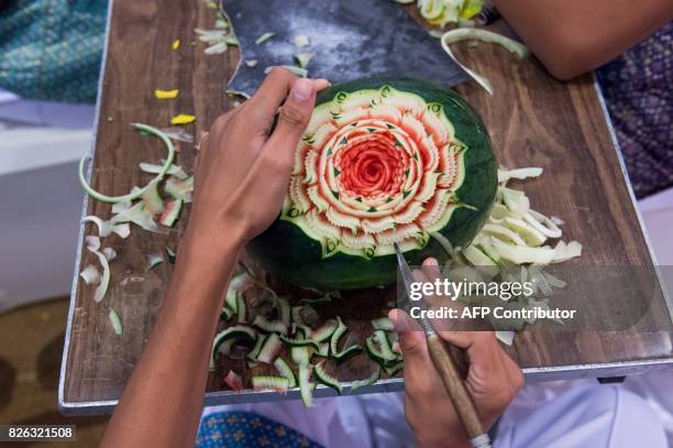 Thai boy carves floral patterns into a watermelon during a fruit and vegetable carving competition in Bangkok on August 4, 2017. It is a royal...