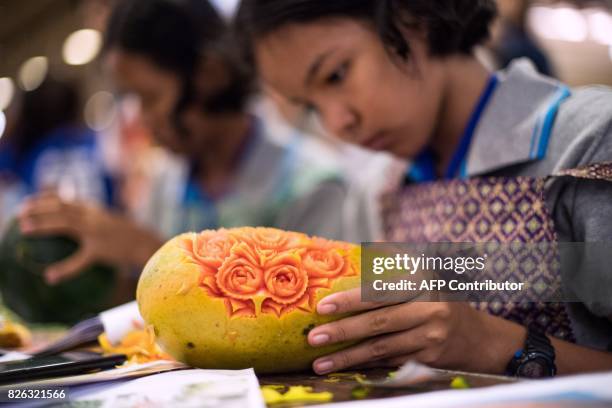 Thai girl carves floral patterns into a papaya during a fruit and vegetable carving competition in Bangkok on August 4, 2017. It is a royal tradition...