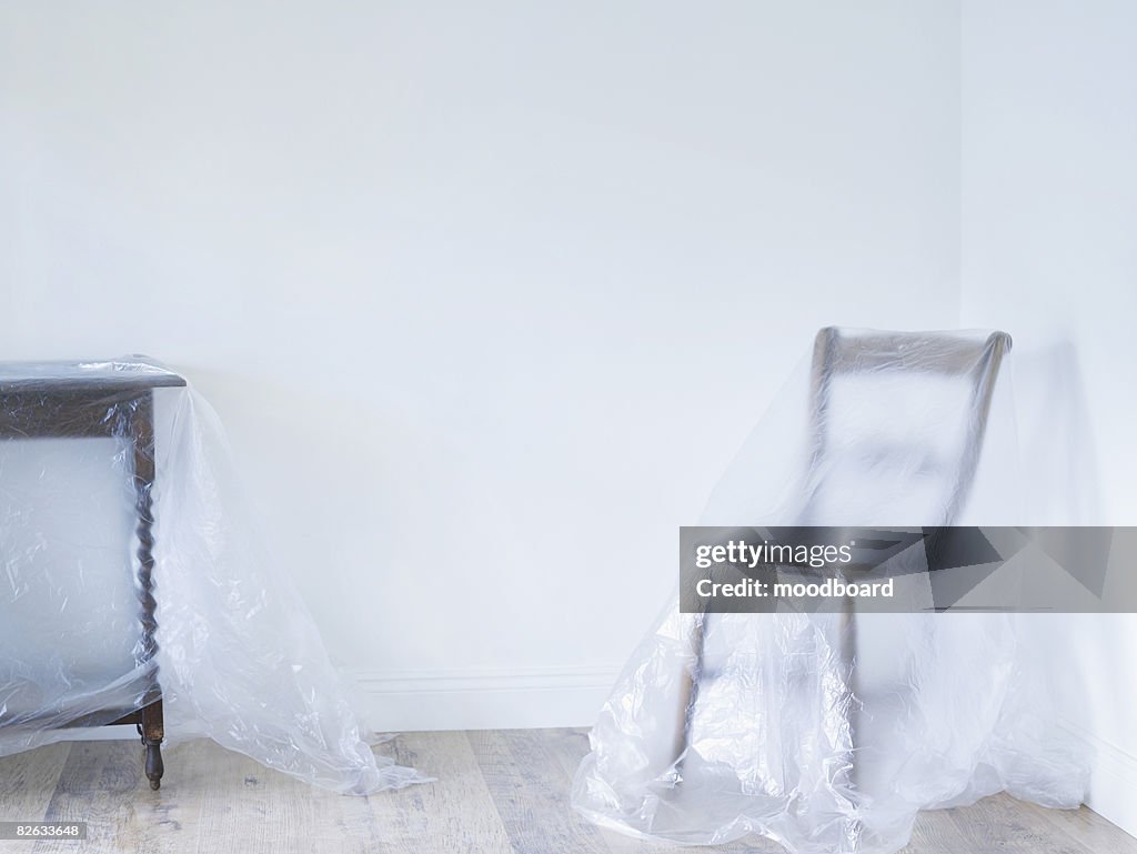 Chair and table covered by plastic in empty room