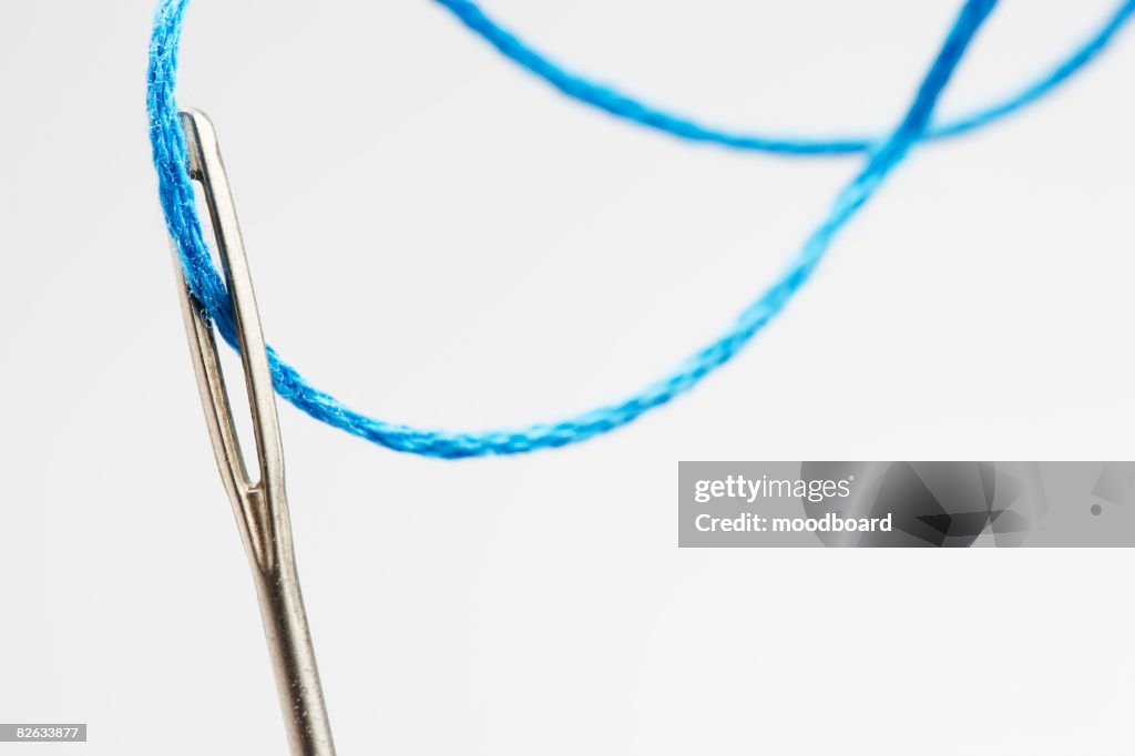 Blue thread going through needle eye, close-up