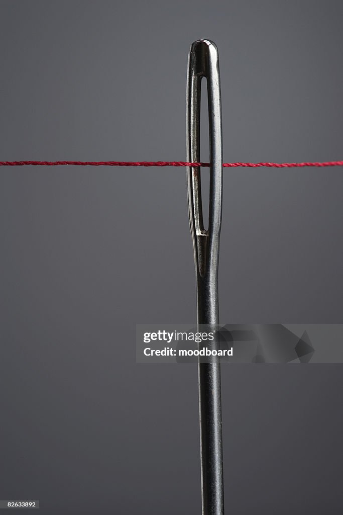 Red thread going through needle eye, close-up