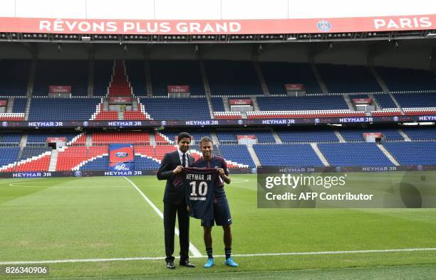 Brazilian superstar Neymar poses with his jersey next to Paris Saint Germain's Qatari president Nasser Al-Khelaifi during his official presentation...