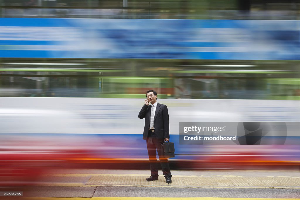China, Hong Kong, business man using mobile phone, standing on street, long exposure