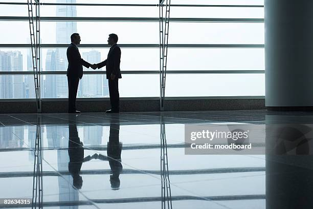 silhouettes of two business men shaking hands - young man asian silhouette stock pictures, royalty-free photos & images