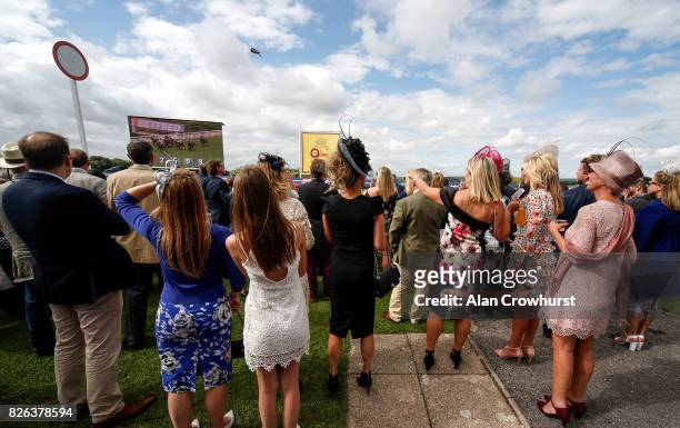 Racegoers stand by the winning post and watch the big screen as the runners approach the finish on day four of the Qatar Goodwood Festival at...