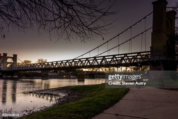 waco, texas feb 24, 2017:  the waco suspension bridge after sunset with lights along the cables illuminated, was taken from the northern bank of the brazos river. - waco stock pictures, royalty-free photos & images