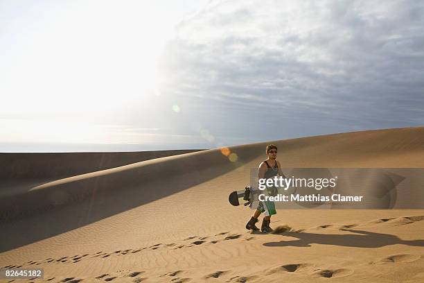 young man walks up a sand dune - sand boarding stock pictures, royalty-free photos & images