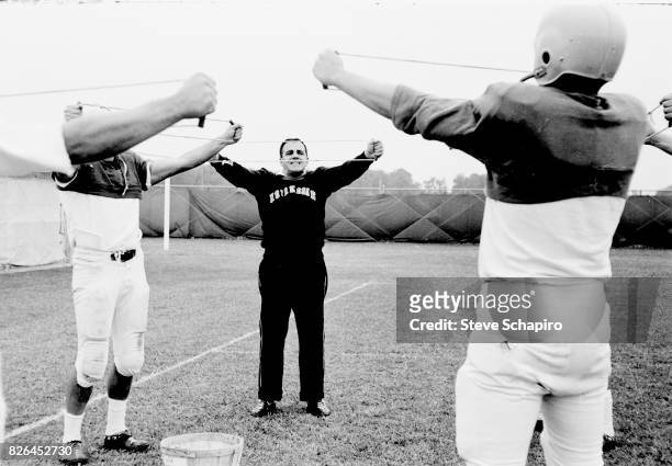 American college football coach Ara Parseghian , of the University of Notre Dame, leads unidentified players in stretching exercises on the field...