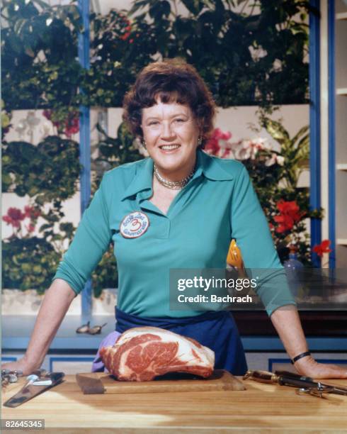 Portrait of the American chef Julia Child shows her standing with a cut of meat in her kitchen, late 20th century.