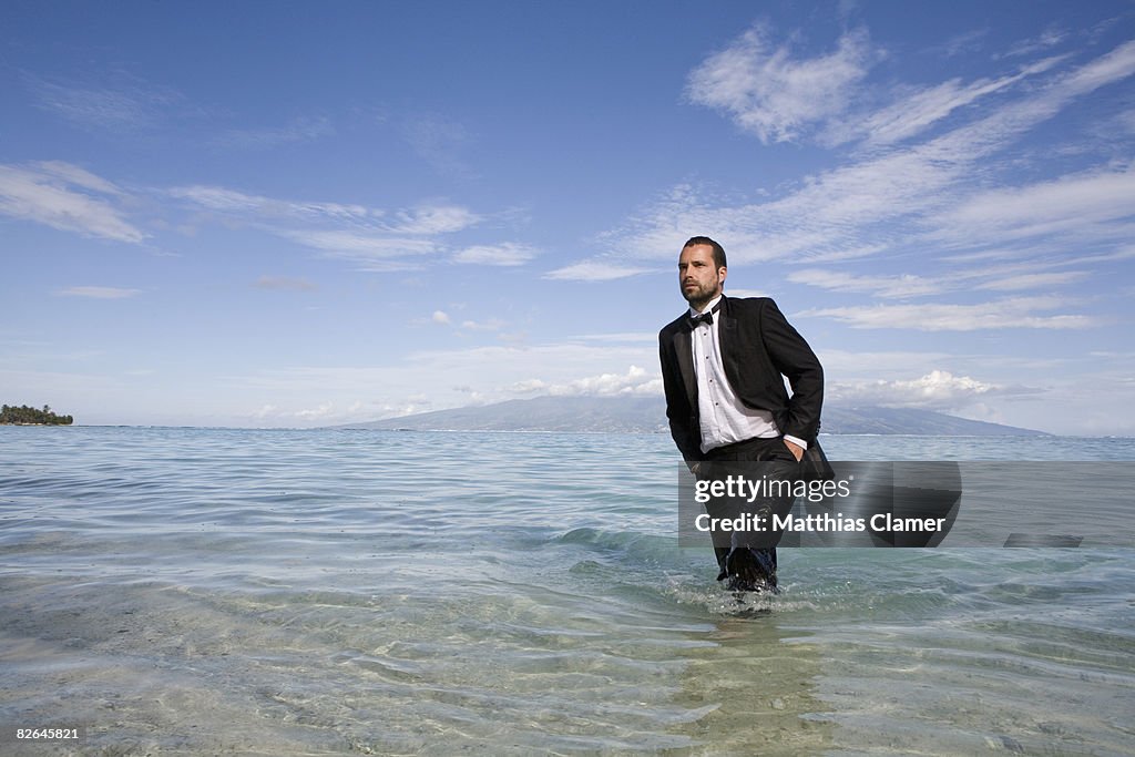 A man stands at shore of blue tropical waters wear