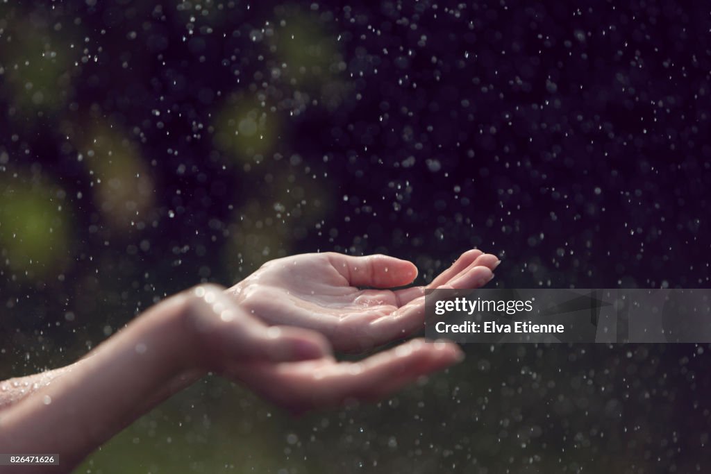 Child catching falling raindrops in hands