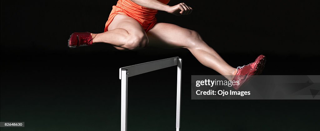 Female runner jumping over hurdle